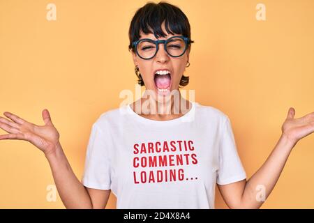Belle femme brunettte portant des commentaires sarcastiques chargement du t-shirt célébrant la victoire avec un sourire heureux et une expression gagnante avec des mains levées Banque D'Images