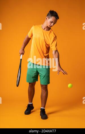 Portrait complet d'un joueur de tennis en action contre arrière-plan orange Banque D'Images