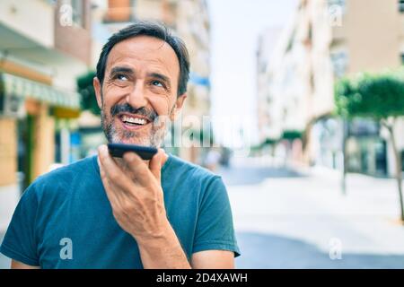 Homme d'âge moyen avec barbe souriante plein air envoi de la voix message sur le téléphone Banque D'Images