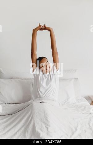 Jeune femme afro-américaine s'étirant au lit à la maison le matin. Banque D'Images