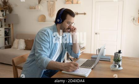 Jeune homme concentré étudiant sur des cours en ligne au bureau à domicile. Banque D'Images