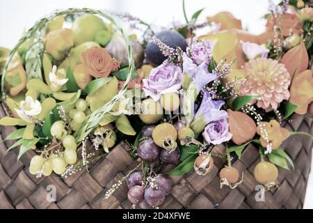 belle décoration composition florale ou bouquet de fruits de saison raisins rosehip dogrosrose et physalis .cerise d'hiver avec de nombreuses fleurs violet orange et vert dans un panier de paille. Banque D'Images