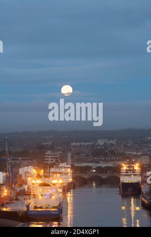 Une pleine lune au-dessus de l'embouchure de la rivière Dee à Aberdeen, en Écosse, avec des navires de soutien pour les plates-formes pétrolières de la mer du Nord amarrés le long des quais Banque D'Images