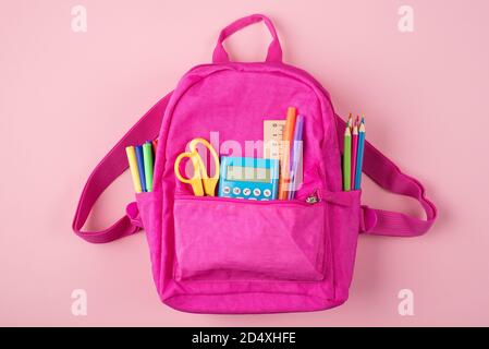 Concept de retour à l'école. Haut au-dessus de la vue de la tête photo de sac à dos rose et de papeterie colorée isolée sur fond rose pastel Banque D'Images