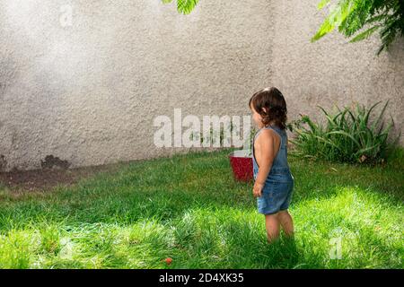 Photo au niveau des yeux d'une petite fille en denim courts-circuits dans un jardin, sous les éclaboussures d'eau Banque D'Images