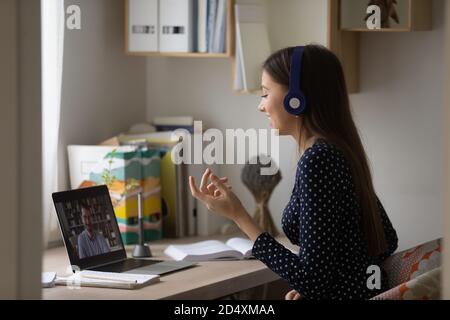 Bonne étudiante féminine impliquée dans une discussion en ligne intéressante avec l'enseignant. Banque D'Images