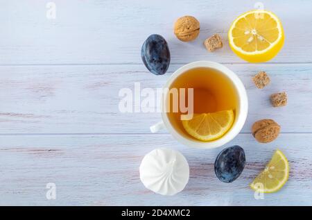 Fond de nourriture avec tasse de thé en porcelaine blanche, citron, prunes et nectarines mûres, noix et guimauves blanches Banque D'Images