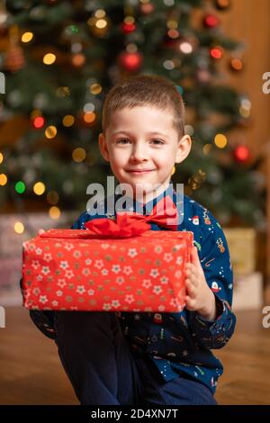 Noël fabuleux, petit garçon tenant une grande boîte rouge avec un cadeau de Santa. Banque D'Images