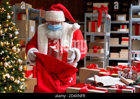 Père Noël portant costume masque de visage emballage cadeaux dans le sac. Livraison en toute sécurité pour Noël. Banque D'Images