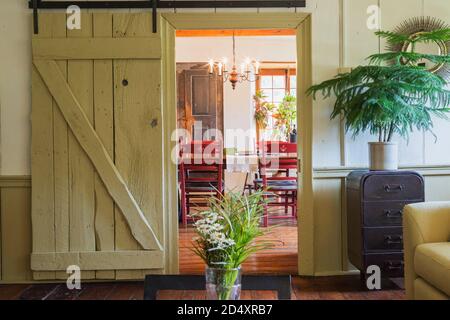 Porte de grange coulissante en bois menant à la salle à manger du salon avec vase de fleur sur table basse à l'intérieur d'une ancienne maison en pierre de style cottage de 1841. Banque D'Images