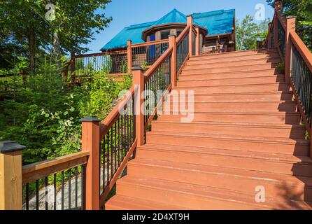 Escalier en bois brun clair teinté avec une banister en fer forgé noir menant à la maison en bois de pin blanc brun blanchi. Banque D'Images