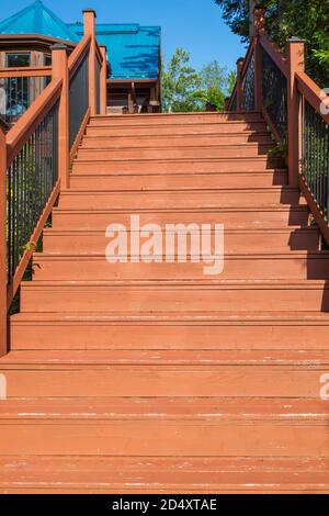 Escalier en bois brun menant au bois de pin blanc de l'est fraisé et à profil plat de la maison en rondins avec toit en tôle à couture verticale bleue en été. Banque D'Images