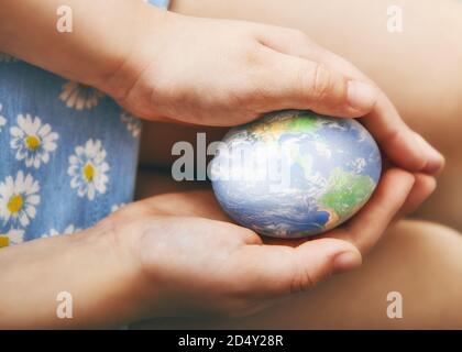 Les mains des enfants tiennent un oeuf de Pâques. L'oeuf a une image du monde. Le concept de paix et de soin au sujet de l'environnement Banque D'Images