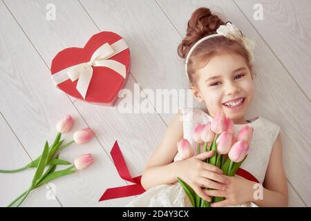 Petite fille douce au coeur rouge et bouquet de tulipes. Bonne petite fille avec le cadeau de la Saint-Valentin couché sur un sol en bois blanc. Mariage, concept de la Saint-Valentin Banque D'Images