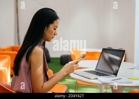 Femme d'affaires asiatique sur le lieu de travail de l'entreprise vérifiant son téléphone mobile sur son bureau. La femme semble inquiète, inquiète, peu concentrée et nerveuse. Banque D'Images