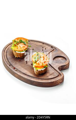 La bruschetta au fromage à la crème de tomates et à l'avocat se trouve sur un panneau en bois. Isolé sur fond blanc. Banque D'Images