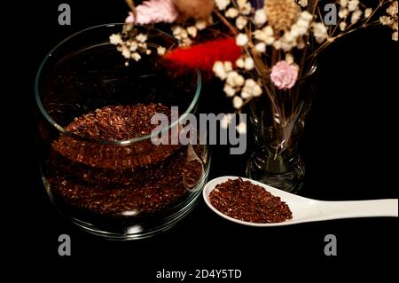 photo verticale d'art de graines de lin dans un pot et cuillère avec un bouquet de fleurs séchées sur un noir arrière-plan Banque D'Images