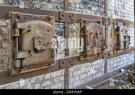 Une rangée de vieilles portes en métal rouillé d'un four en brique rouge dans une usine abandonnée. Vieilles portes à hayon rouillées avec cadres métalliques boulonnés à l'ancien mur de briques rouges Banque D'Images