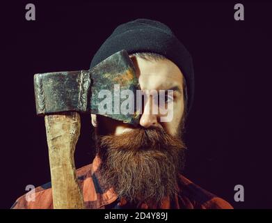 Bel homme ou bûcheron, hipster barbu avec barbe et moustache en hat détient old rusty lame de fer d'ax isolé sur fond noir Banque D'Images