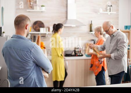 Homme qui arrive à la maison avec un sac de papier d'épicerie du supermarché. Bonne bonne grande famille pour préparer un savoureux brunch. Homme senior tenant une bouteille de vin. Banque D'Images