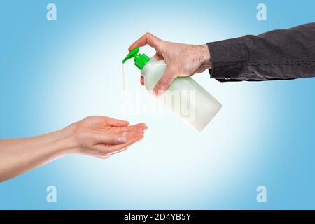 La main d'un homme goutte du savon antibactérien pour la désinfection des paumes des femmes. Arrière-plan bleu clair. Copier l'espace. Concept d'une pandémie virale, protection fr Banque D'Images