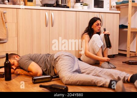 Une femme maltraitée boit de l'alcool près d'un mari ivre et abussif dans la cuisine. Alcoolique agressif homme abusant blessant femme terrifiée, peur, battue et paniquée. Banque D'Images