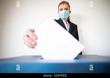 femme portant un masque mettant le vote au scrutin Banque D'Images