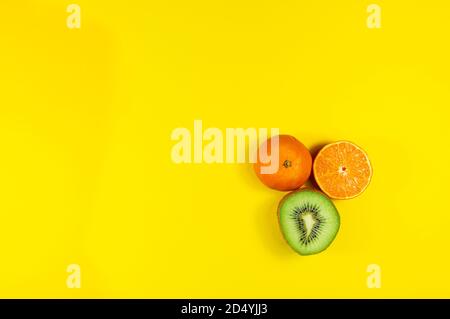 Mandarine entière, demi-mandarine et demi-kiwi isolés sur fond jaune Banque D'Images