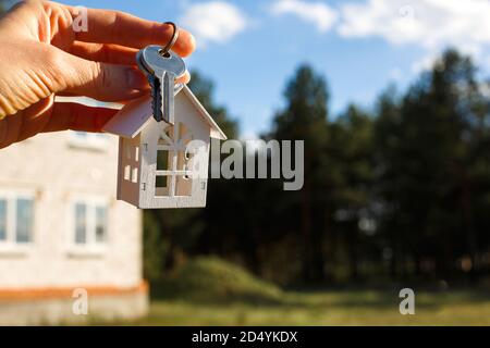 Porte-clés en bois et clés à portée de main sur le fond d'une maison inachevée. Rêve de se déplacer, le cottage est dans un emplacement rural et l'achèvement de la Banque D'Images