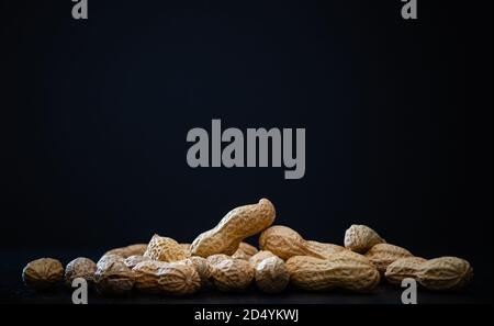 Cacahuètes avec coquille sur fond noir - photographie de nourriture sombre Banque D'Images