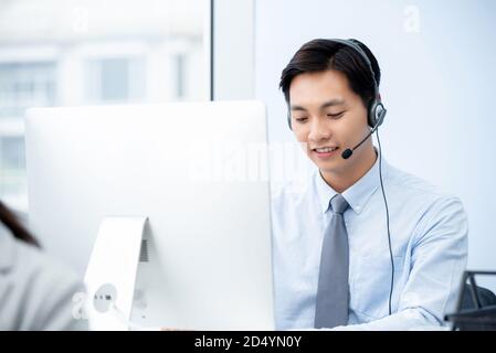 Le personnel de télémarketing asiatique souriant de sexe masculin porte un micro-casque qui fonctionne dans le bureau du centre d'appels Banque D'Images