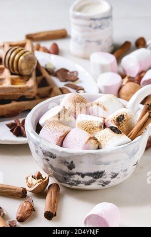 Tasse en céramique de chocolat chaud avec de la guimauve avec des s'mores gaufrettes au miel et des ingrédients ci-dessus en marbre blanc sur table. Boisson d'hiver. Close up Banque D'Images