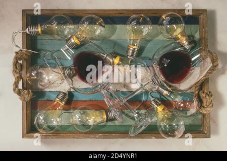 Deux verres de vin rouge et rétro éclairé avec guirlande de noël lampes en plateau en bois sur fond de marbre blanc. Mise à plat, de l'espace Banque D'Images