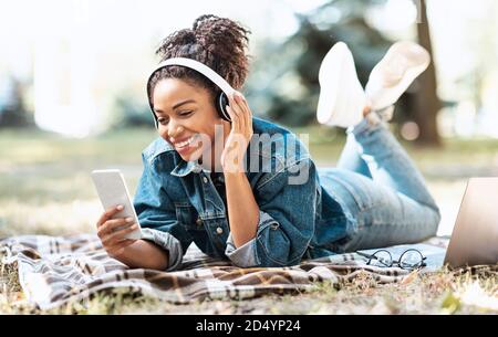 Black Lady utilisant le téléphone et les écouteurs écouter de la musique en plein air Banque D'Images