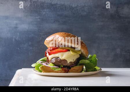 Close up of burger classique maison en pain de blé à partir de boeuf et de veau de lait, de fromage fondu et les légumes sur le conseil en céramique blanche sur l'onglet en marbre blanc Banque D'Images