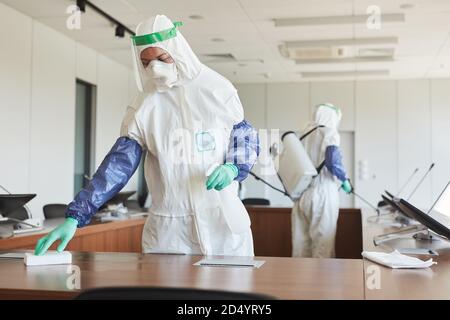 Portrait de deux travailleurs de l'assainissement portant des combinaisons de matières dangereuses pour le nettoyage et la désinfection de la salle de conférence dans le bureau, l'espace de copie Banque D'Images