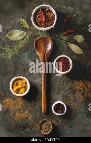 Assaisonnement épices et herbes diverses dans des bols en céramique. La masse différents poivrons, piment, curcuma, feuilles de laurier, la cannelle et cuillère en bois foncé sur m Banque D'Images