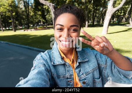 Une femme africaine positive élève faisant le geste de Selfie victoire-signe dans le parc Banque D'Images