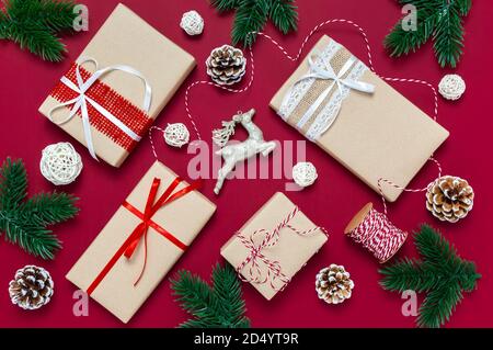 Boîtes-cadeaux de Noël faites à la main, cornets de pin, branches d'arbre et renne sur fond rouge, vue de dessus, plat. Emballage des cadeaux de Noël Banque D'Images