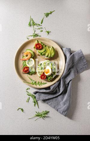 Variété de sandwiches végétariens avec des tranches d'avocat, de tomates, oeufs, crevettes, roquette servis sur une plaque en céramique blanc tacheté de gris zone Banque D'Images