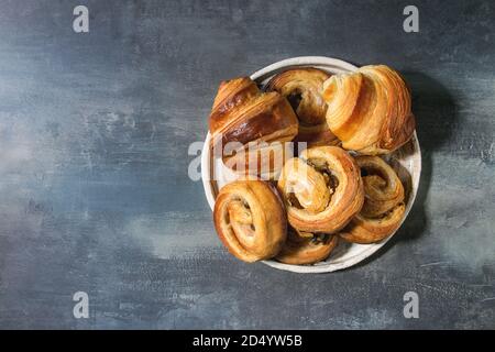 Variété de pâte feuilletée faite maison à la cannelle brioches et croissants servis dans une plaque en céramique bleu sur fond de texture. Mise à plat, de l'espace Banque D'Images