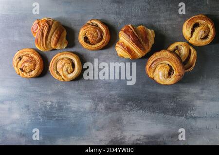 Variété de pâte feuilletée faite maison à la cannelle brioches et croissants dans la rangée sur blue texture background. Mise à plat, de l'espace Banque D'Images