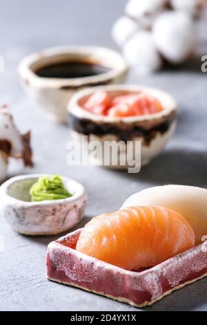 Set à Sushi nigiri de saumon et en céramique rose butterfish plat de service avec des bols de sauce soja et de gingembre mariné, fleurs de coton sur l'onglet bleu clair Banque D'Images