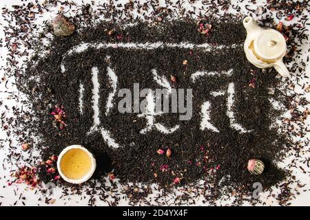 Inscription calligraphique lettres gothiques sur thé noir ceylan sec et thé vert éparpillés sur du marbre blanc avec boutons de rose, ceramik théière et tasse. Plateau Banque D'Images