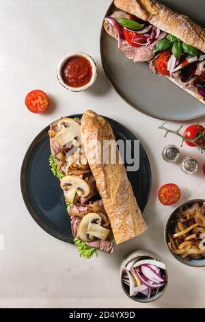 Variété de sandwichs baguette boeuf avec champignon champignons, salade verte, tomates, oignon frit servi sur une plaque en céramique avec des ingrédients ci-dessus sur Banque D'Images