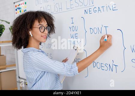 Enseignant pour l'éducation en ligne. Une femme afro-américaine attrayante écrit des règles anglaises sur un tableau blanc Banque D'Images