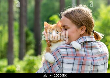 Gros plan de la femme souriante dans une chemise à carreaux embrassant et embrassant avec tendresse et amour domestique excitée triste chat dehors. L'amour pour les animaux, les animaux de compagnie Banque D'Images