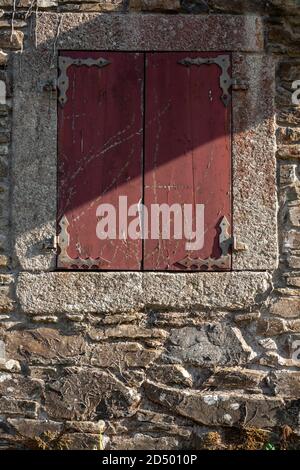 Fenêtre espagnole en bois rouge avec volets et cadre en pierre. Construction architecture maison de campagne rustiques en pierre. Banque D'Images