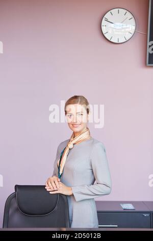 Portrait vertical d'une jeune femme élégante regardant l'appareil photo tout en s'appuyant sur une chaise dans le bureau contre le mur violet, espace de copie Banque D'Images