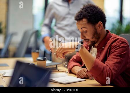 Problèmes d'entreprise. Jeune homme de race mixte frustré et triste, assis à son bureau et travaillant dans le bureau moderne. Travail stressant Banque D'Images